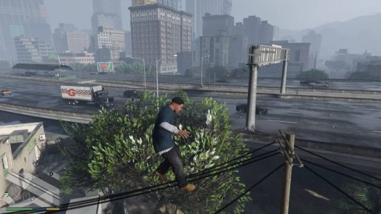 GTA 5 cheats - Franklin is jumping extremely high into the air, clearing the telephone cables and tree behind him. There is also a freeway and tall buildings behind him.