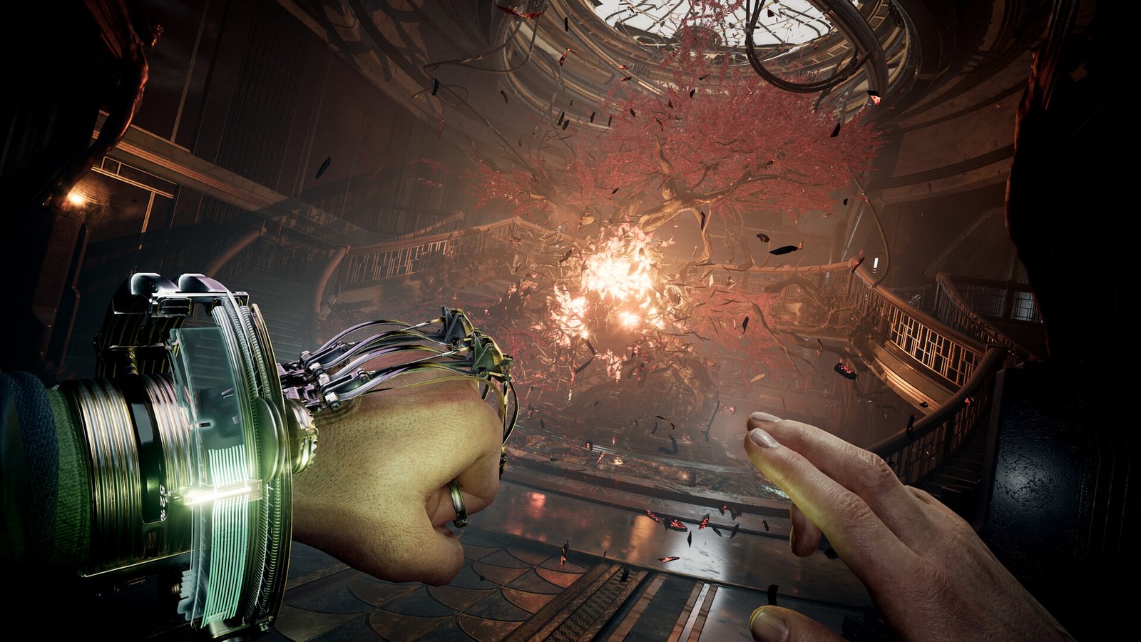 A man reaches out towards a burning cherry blossom tree in an atrium area wearing an odd metal glove